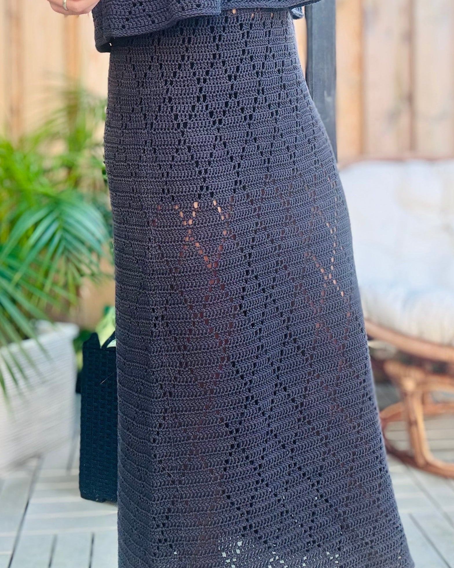 Person wearing a dark gray crochet outfit standing outdoors.